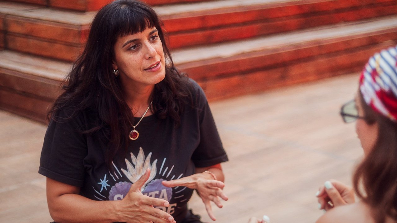 Lore Ferreyra conversando con una alumna, sentadas en un deck de madera